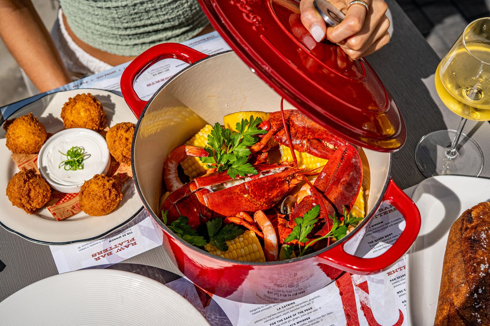 A red dutch oven brimming with whole lobster, shrimp, clams and corn